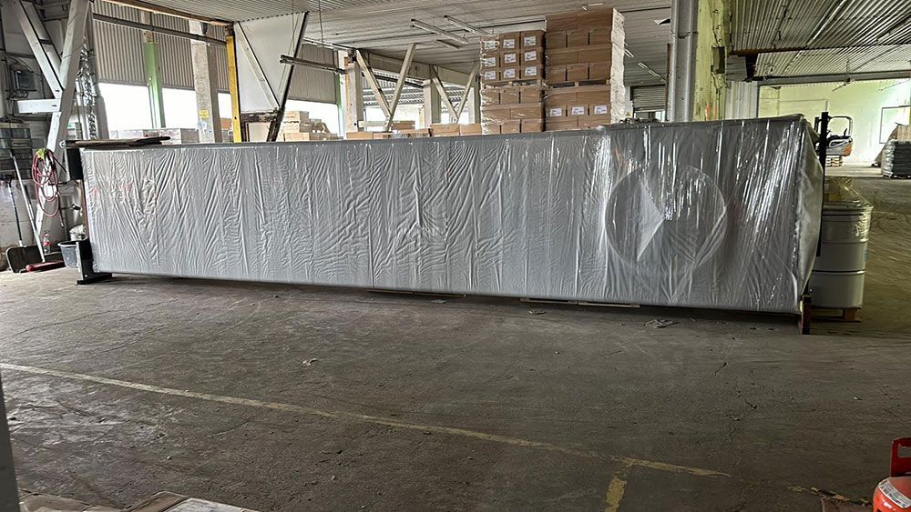 In einer Lagerhalle wird eine große Metallkonstruktion in Plastik eingewickelt.