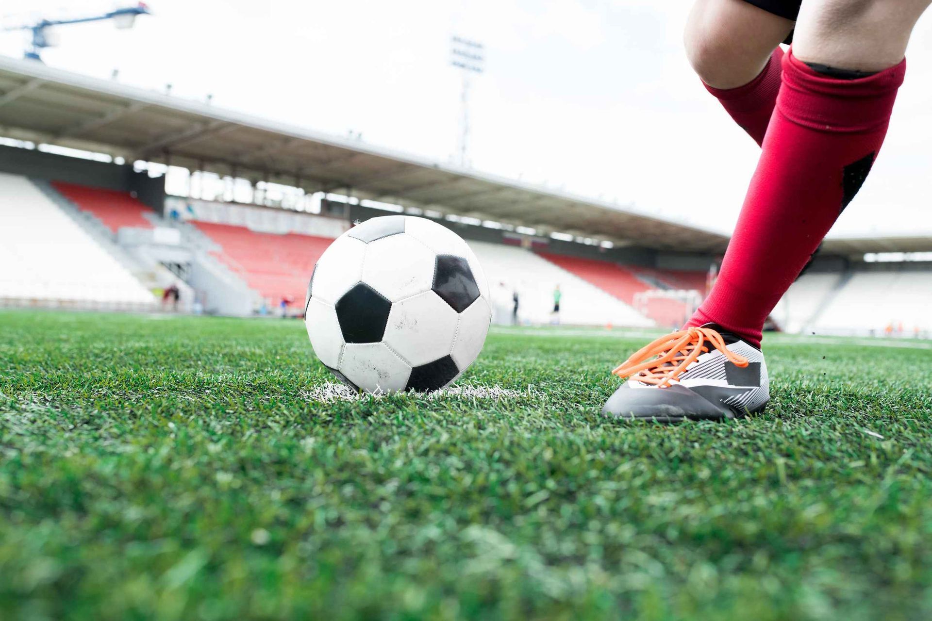 Jugador de fútbol pateando un balón en un campo verde frente a las gradas del estadio.