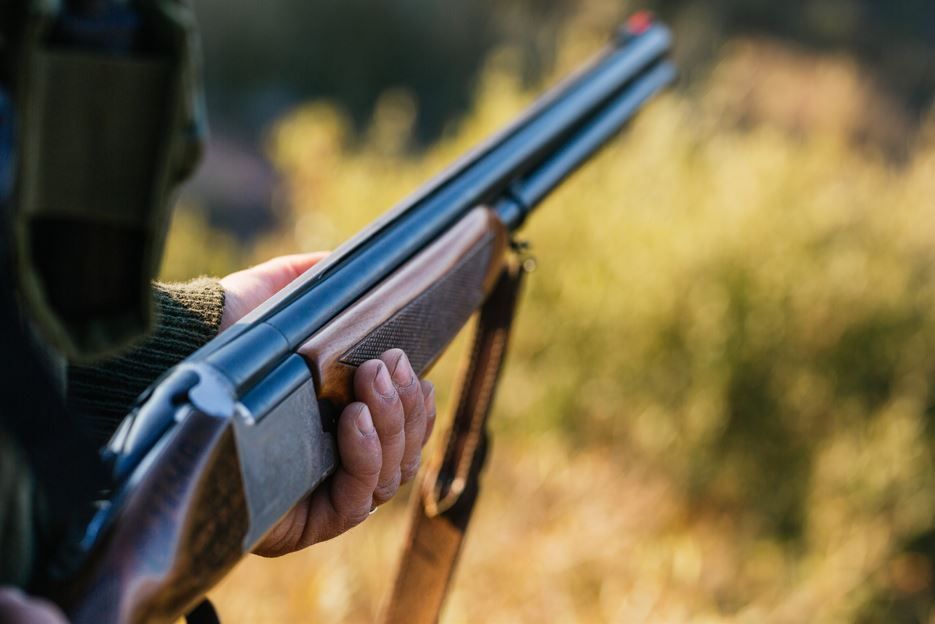 Una escopeta sobre una mesa en una oficina, con dos hombres borrosos al fondo, sentados a un escritorio.