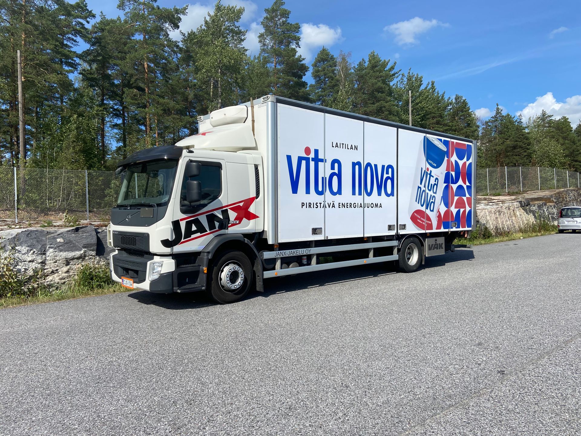 Valkoinen Vita Nova -umpikorikuorma-auto pysäköitynä soratielle puiden viereen sinisen taivaan alla
