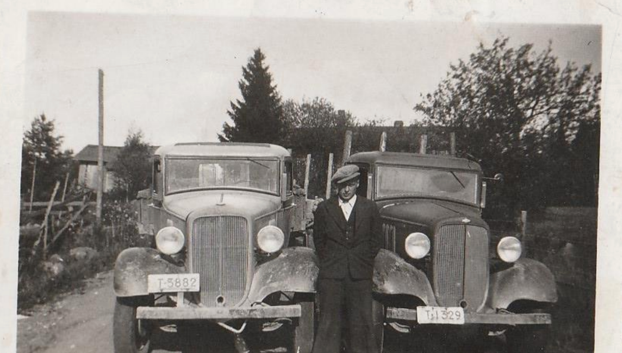 Kaksi vierekkäin pysäköityä vanhaa autoa, joiden välissä ulkona henkilö seisoo