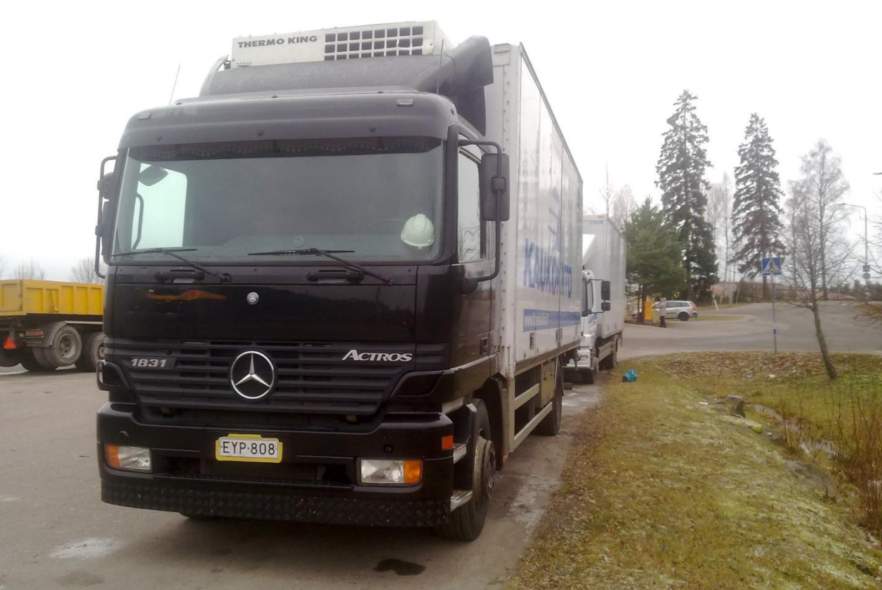 Musta Mercedes Actros -umpikorikuorma-auto pysäköitynä tien varteen ruohon ja puiden viereen