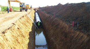 Se está instalando una tubería de gran tamaño en una zanja al lado de una carretera.