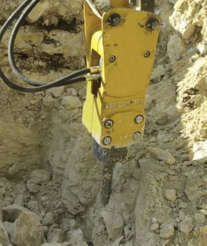 Una máquina amarilla está rompiendo rocas en un montón de tierra.