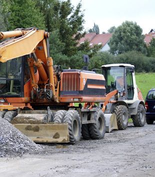 Un tractor y una excavadora están estacionados uno al lado del otro en un camino de tierra.