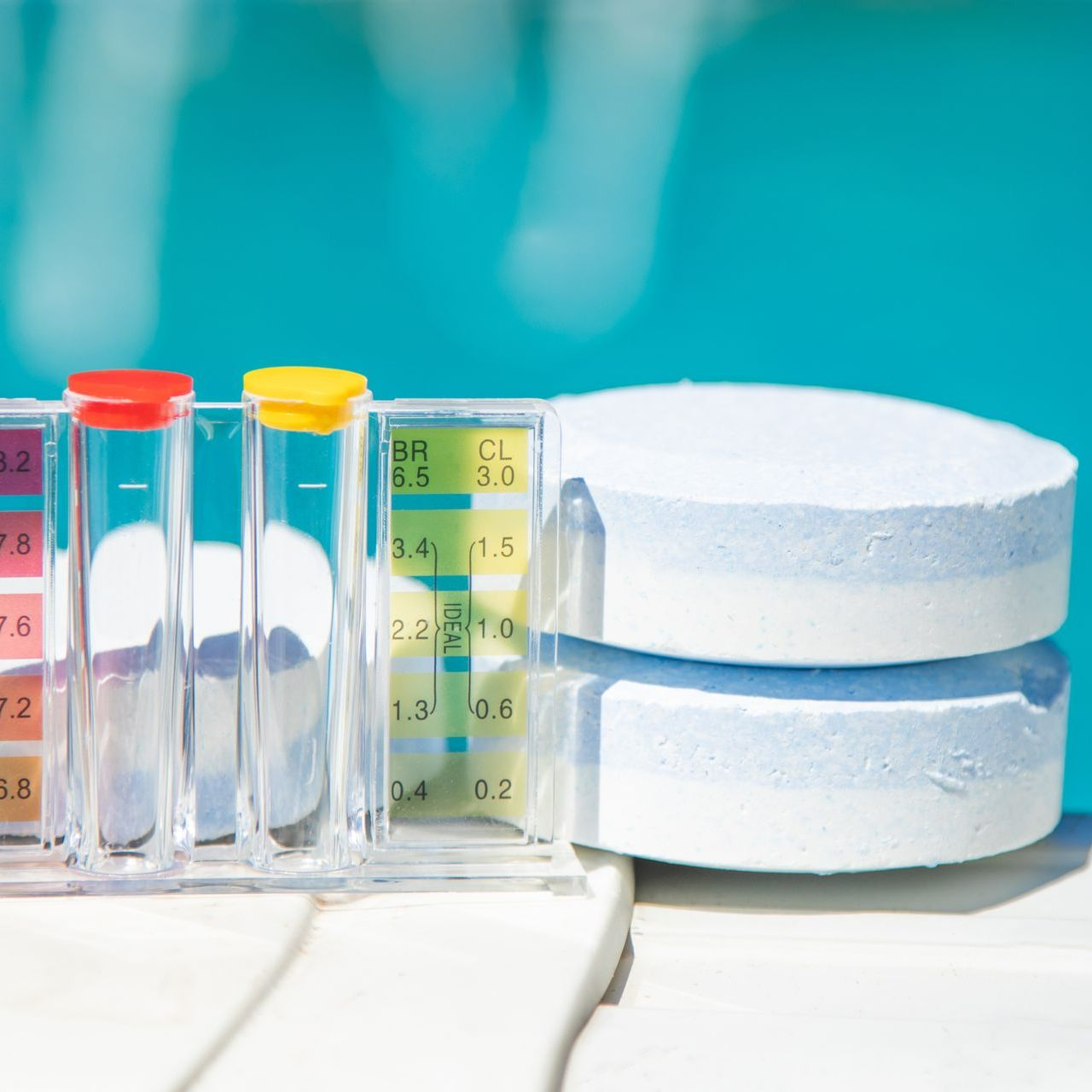 Galets de chlore et testeur de pH posés sur le bord d'une piscine