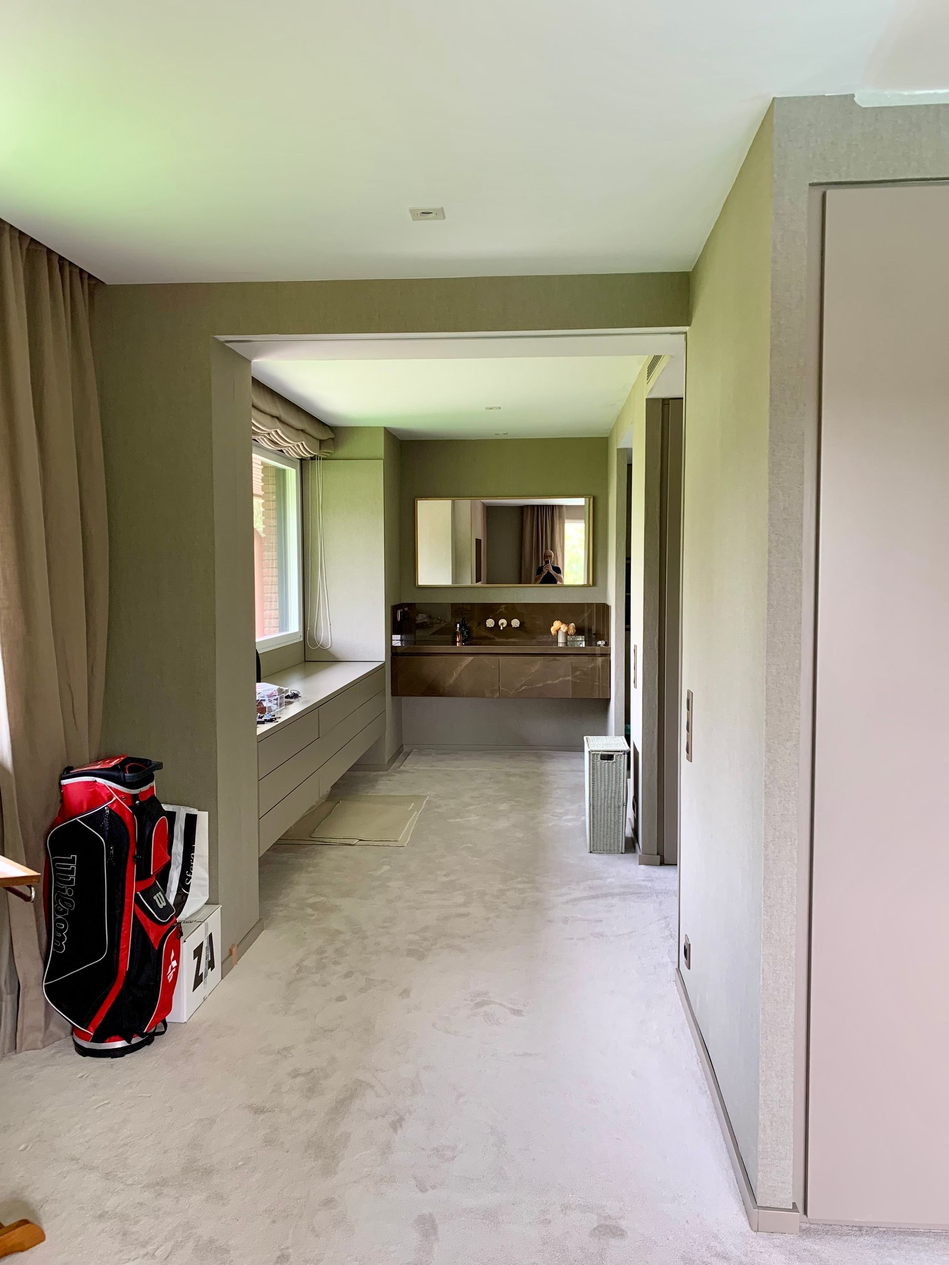Una bolsa de golf roja está en un pasillo que conduce a un baño.
