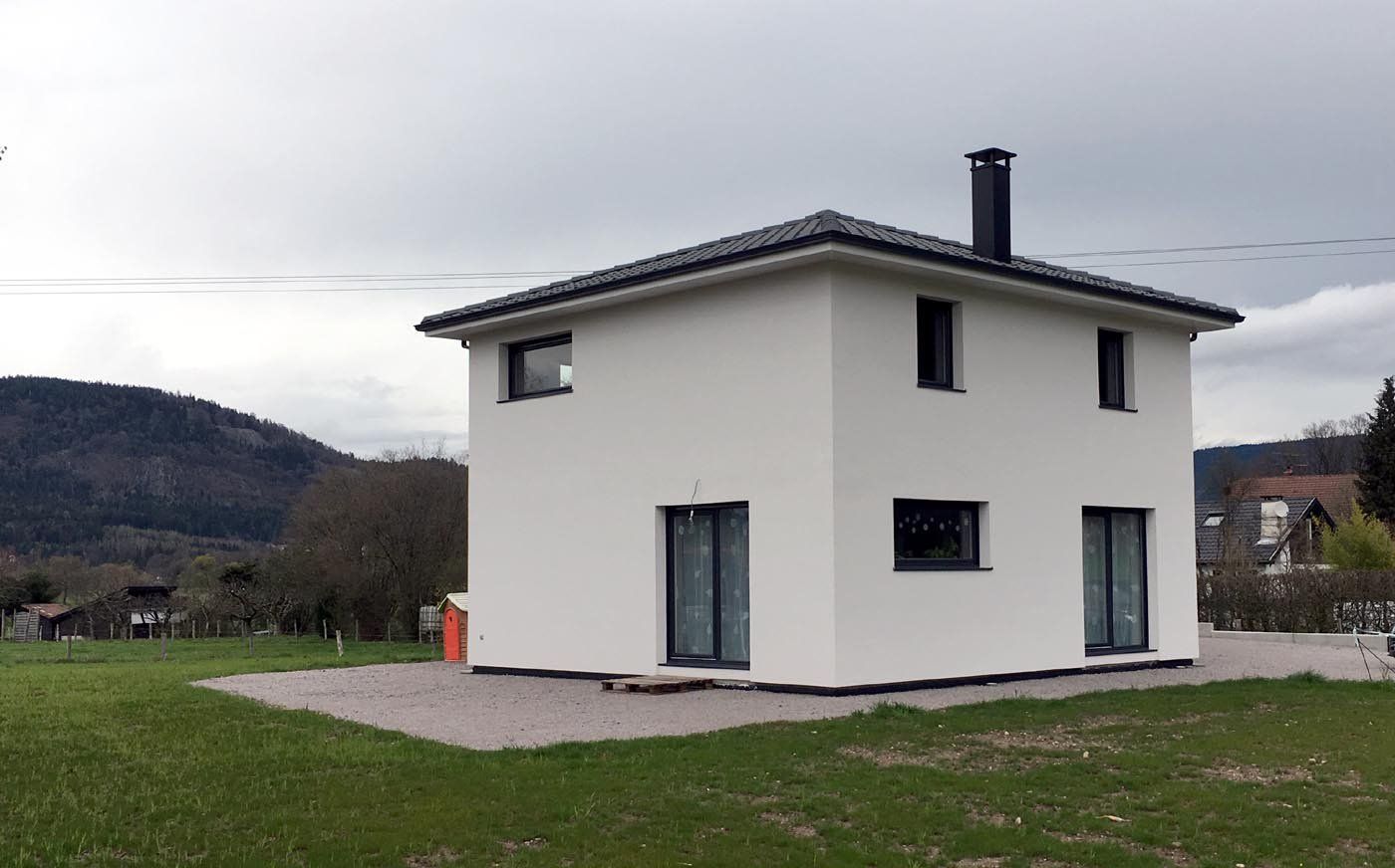 Maison moderne blanche de deux étages avec toit foncé dans un cadre rural herbeux