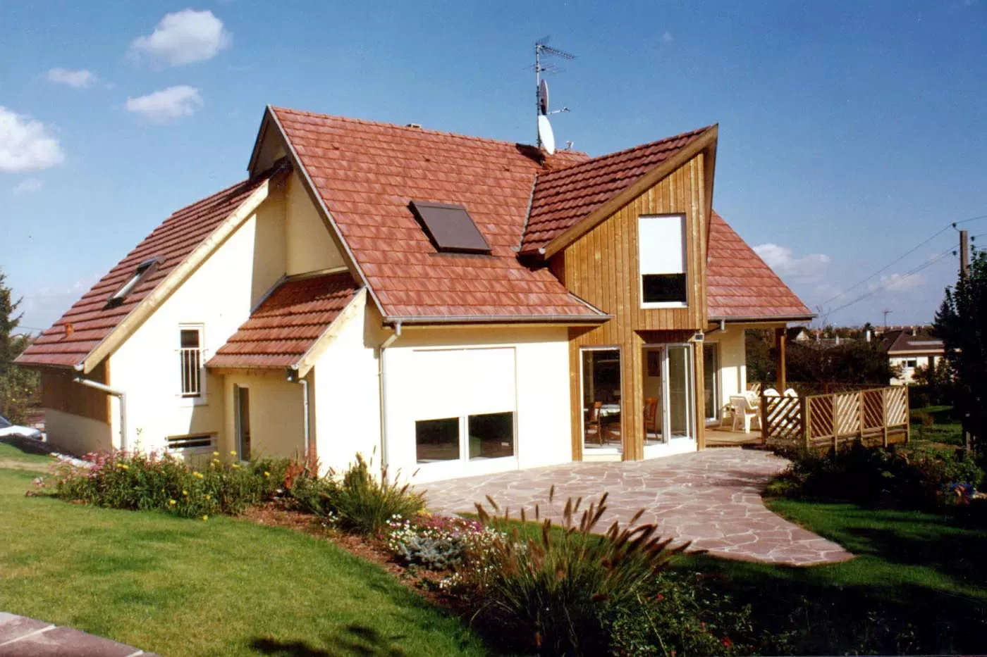 Maison moderne avec toit de tuiles rouges, garage et jardin dans une cour ensoleillée