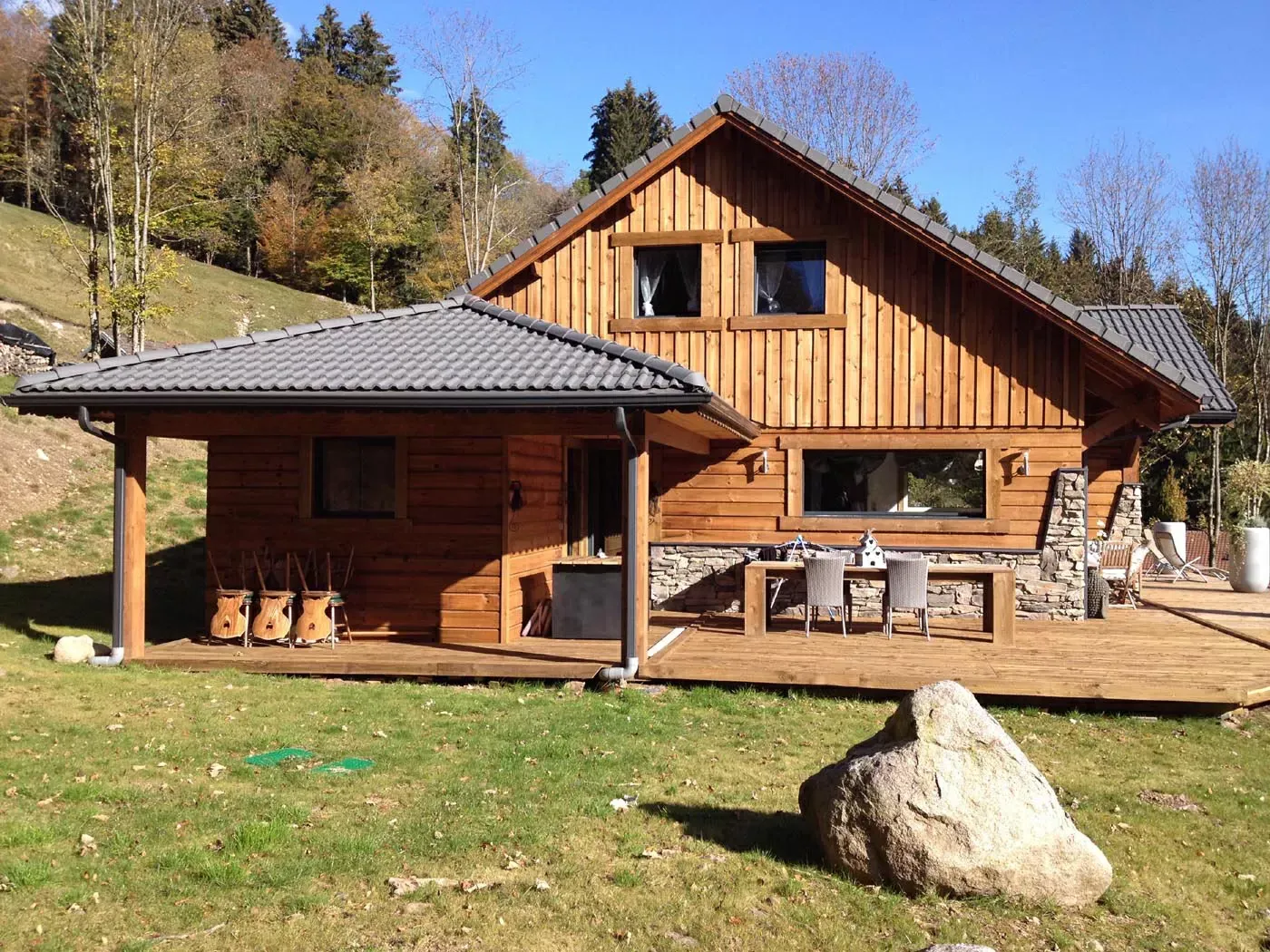 Cabane en bois avec porche et cheminée en pierre sur un flanc de colline herbeux sous un ciel dégagé
