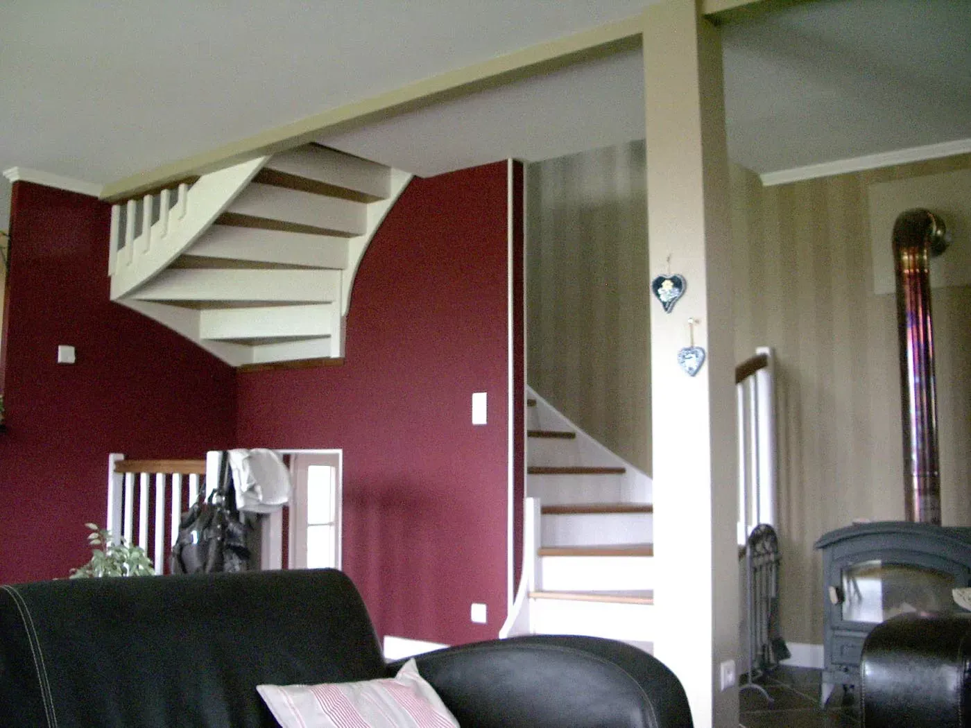 Salon avec mur bordeaux, escalier en colimaçon blanc et poêle à bois