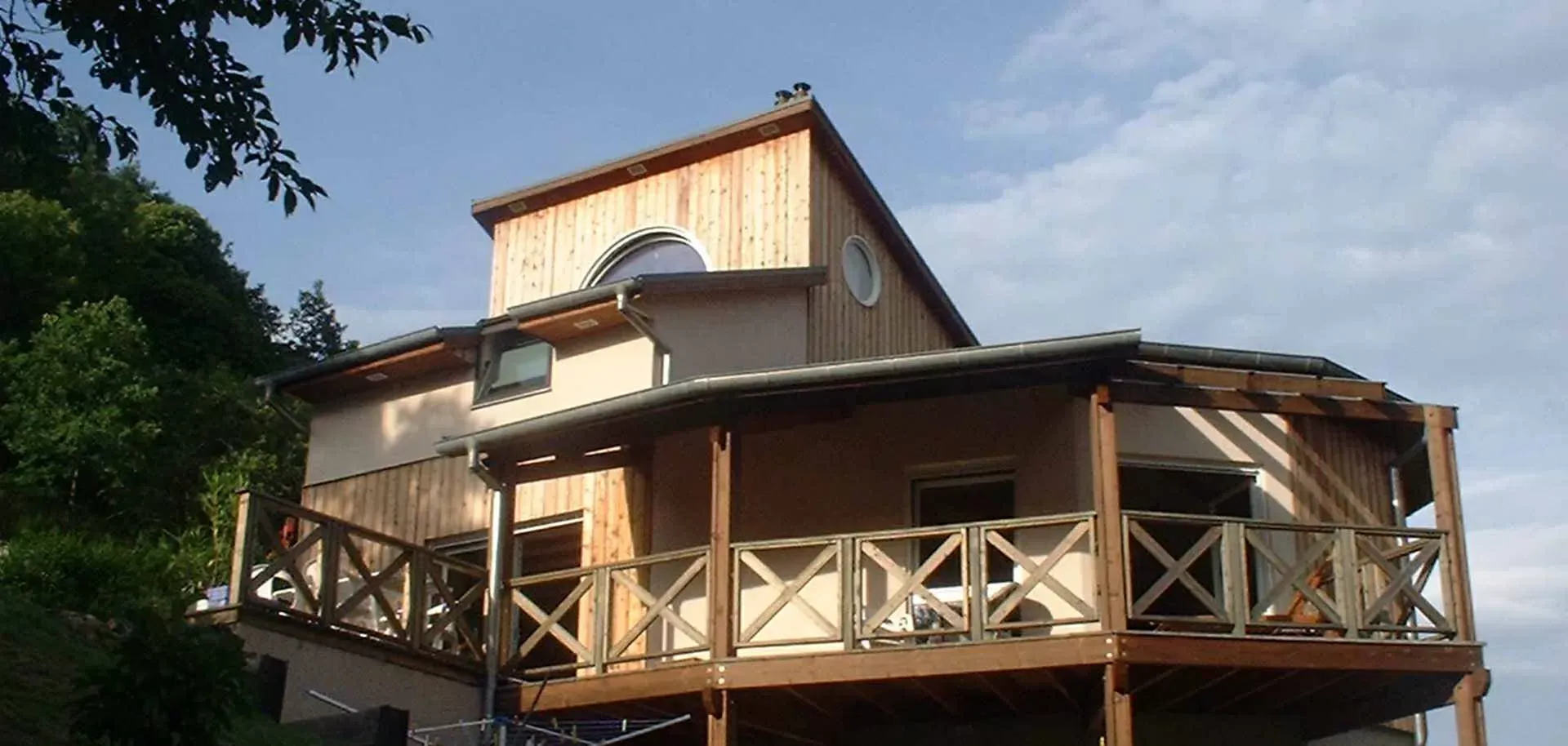 Maison en bois avec véranda enveloppante et balustrades blanches sur un versant ensoleillé