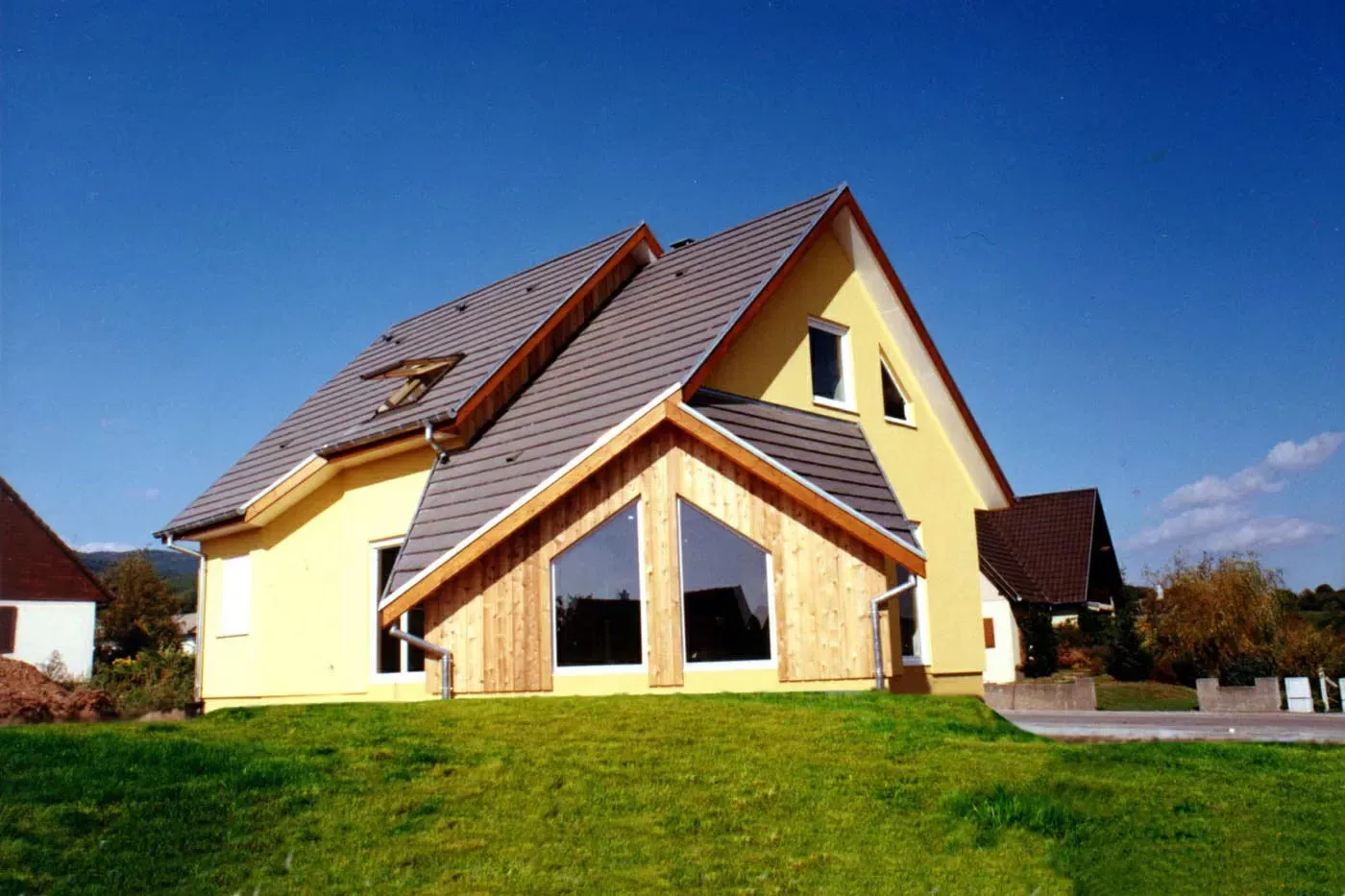 Maison jaune au toit rouge et aux grandes fenêtres sur une pelouse sous un ciel bleu