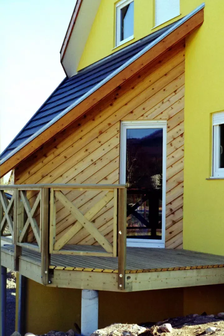 Balcon et porte en bois sur une maison jaune au toit en pente et aux finitions bleues