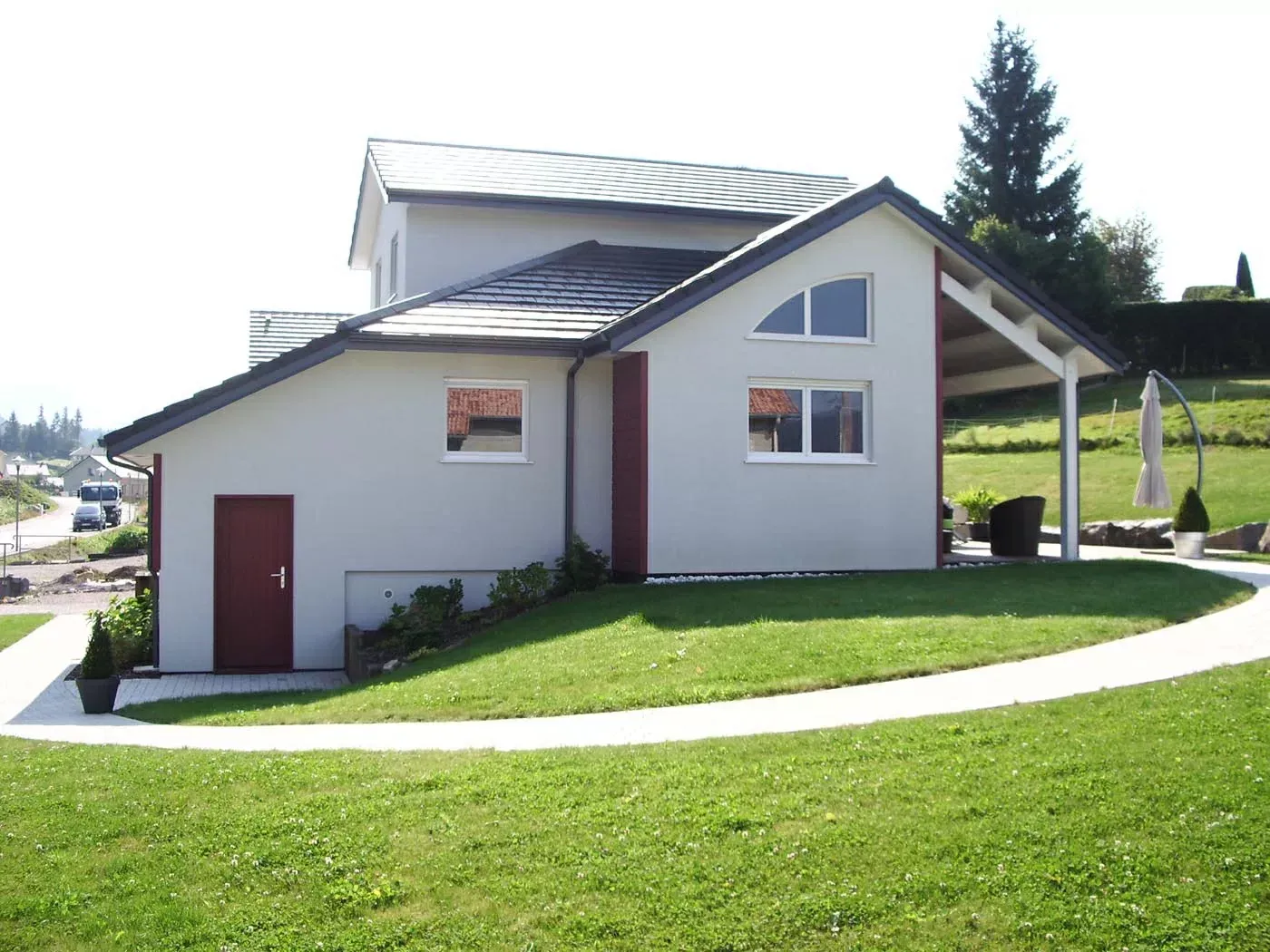 Petite maison blanche au toit en pente, sur un flanc de colline herbeuse, avec une porte et des fenêtres rouges.