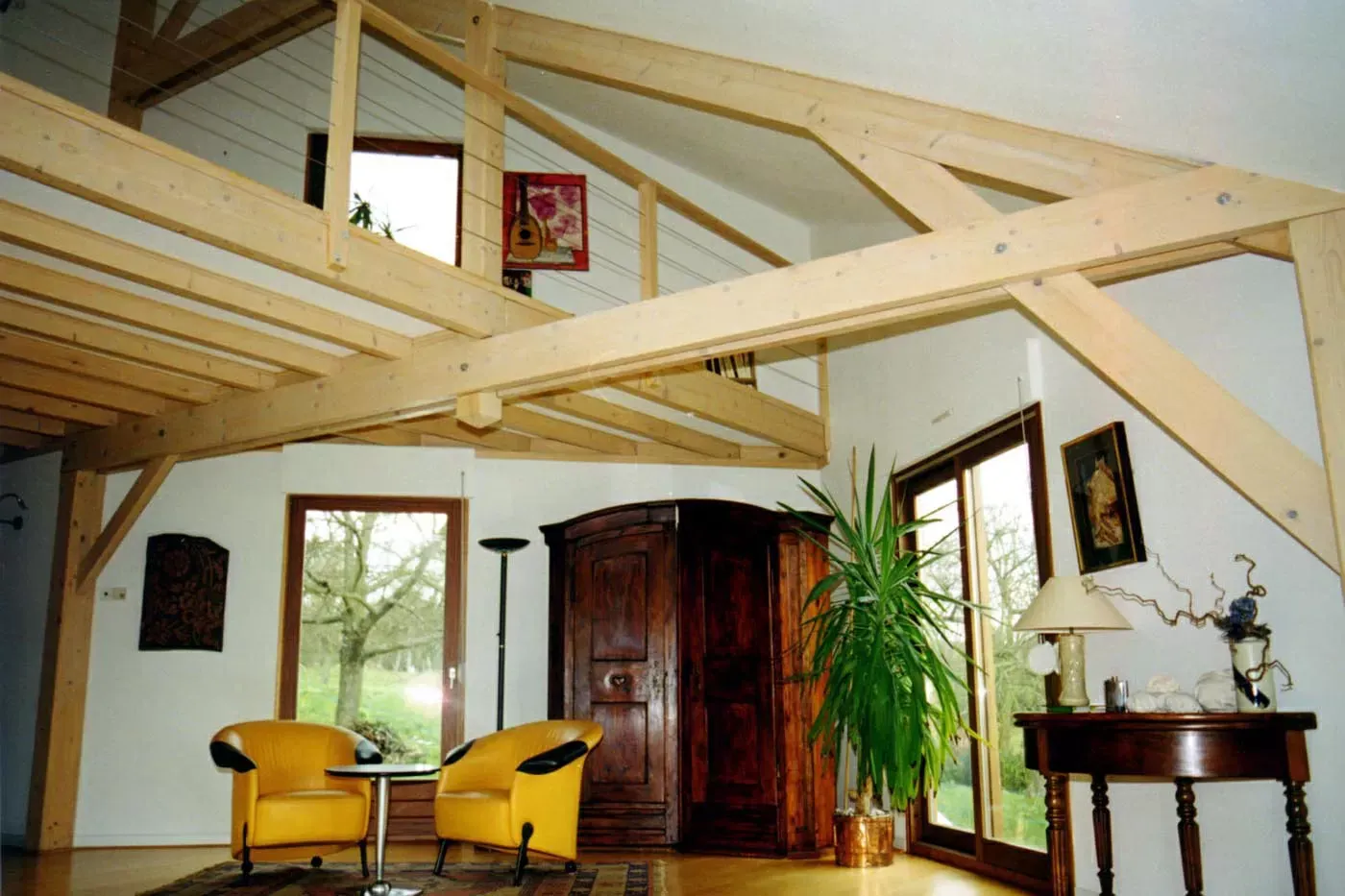 Salon rustique de style loft avec poutres apparentes, chaises jaunes, armoire en bois et grande plante en pot.
