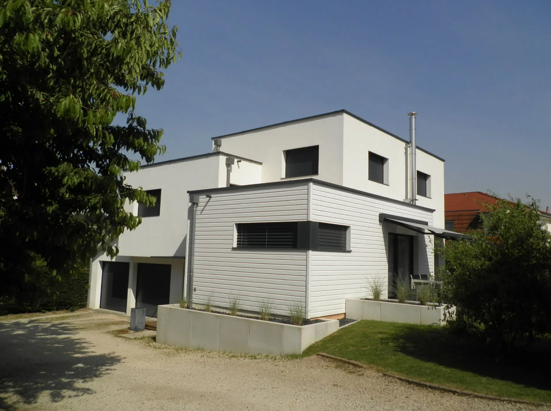 Maison moderne blanche à deux étages avec un auvent rayé, un garage et une allée de gravier sous un ciel bleu