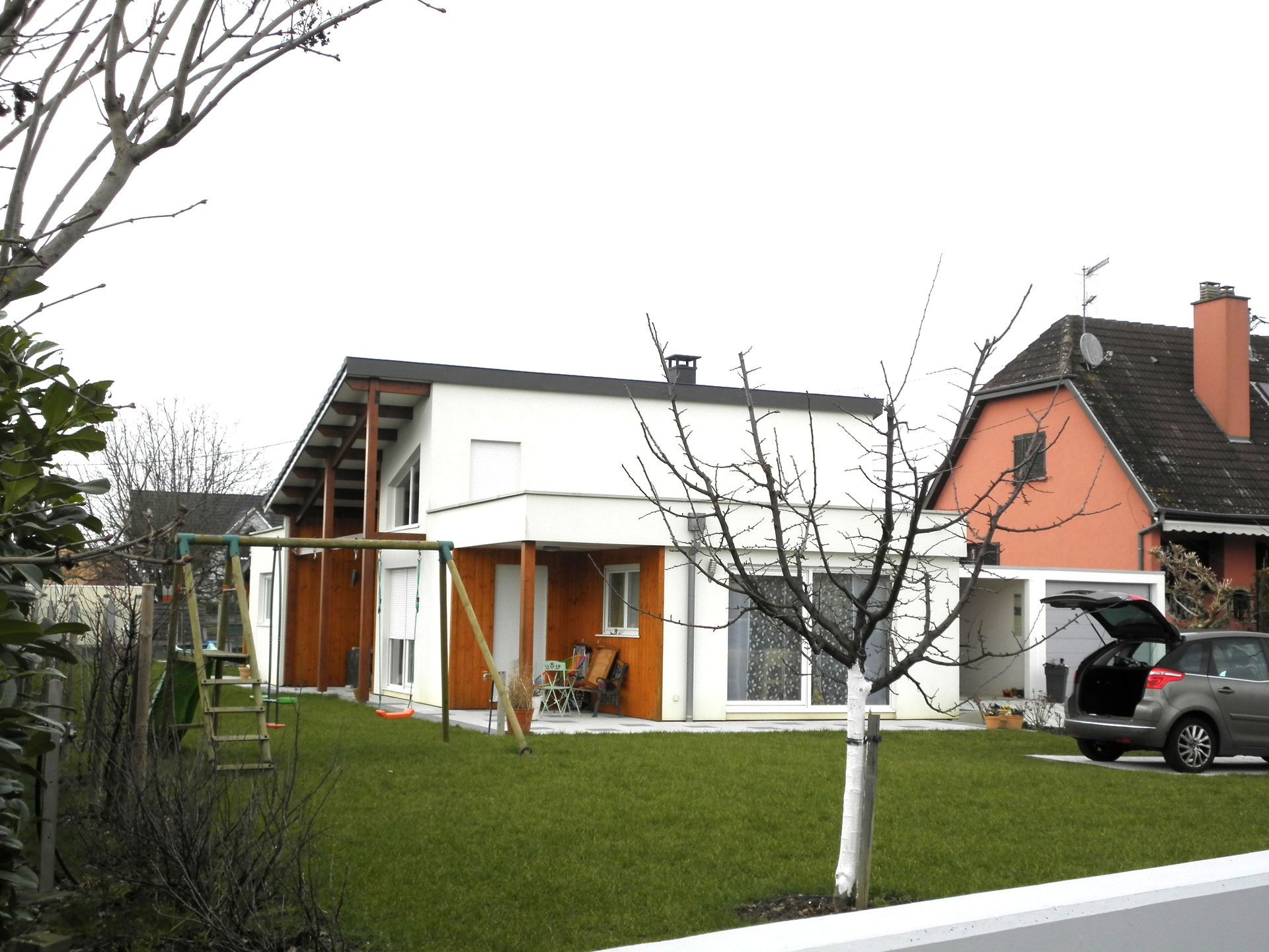 Maison blanche moderne avec des touches d'orange, une pelouse verte et un SUV garé dans l'allée.
