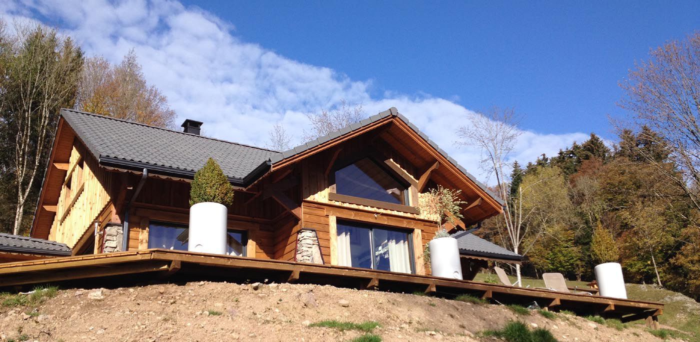 Cabane en bois à flanc de colline avec des réservoirs blancs, sous un ciel bleu et des arbres aux couleurs d'automne
