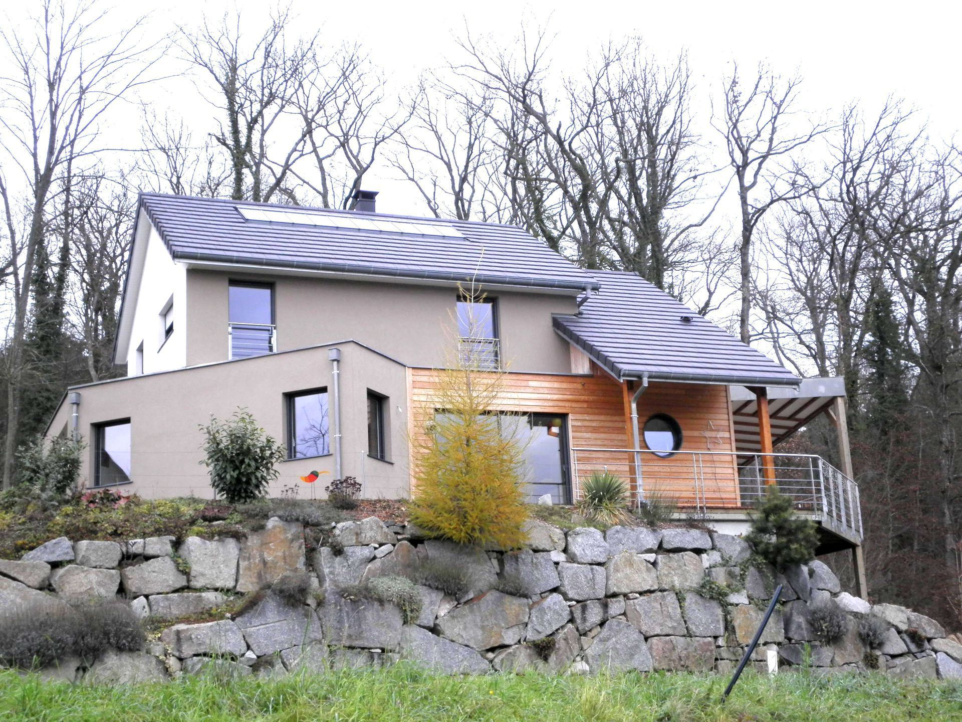 Maison moderne avec fondations en pierre, porche éclairé et arbres dénudés en arrière-plan