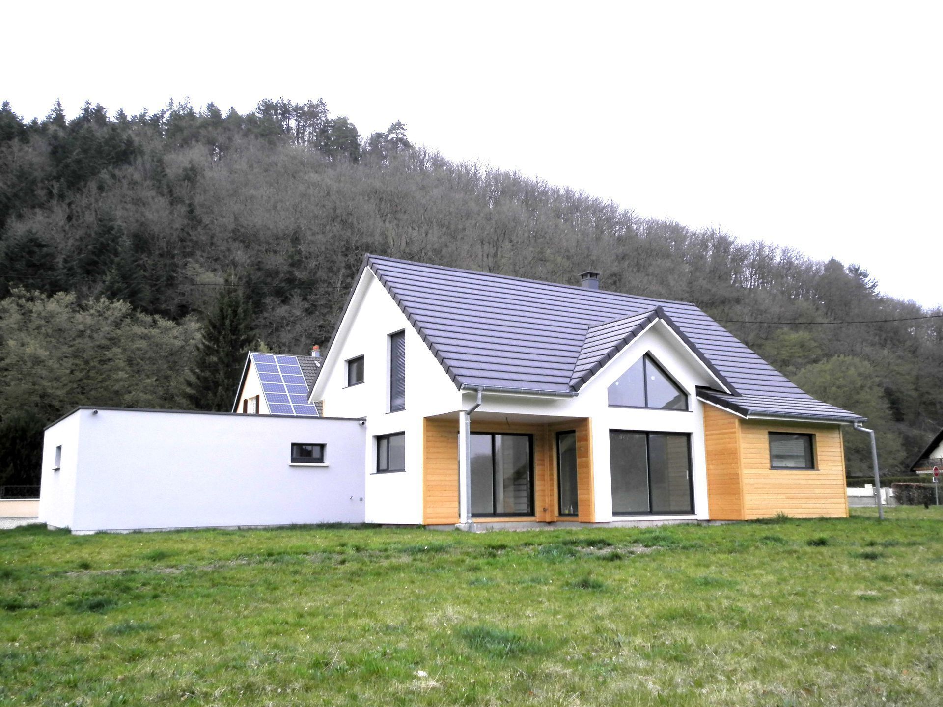 Maison moderne à l'extérieur blanc et en bois sur un coteau herbeux près d'une forêt