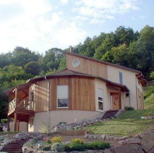 Maison moderne à flanc de colline avec bardage en bois, marches en pierre et arbres en arrière-plan