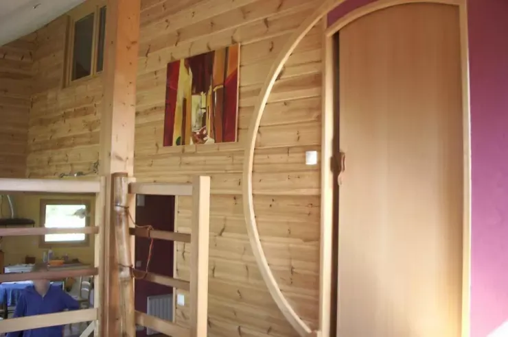 Intérieur lambrissé avec lits superposés, un petit tableau mural et une porte en bois cintrée.