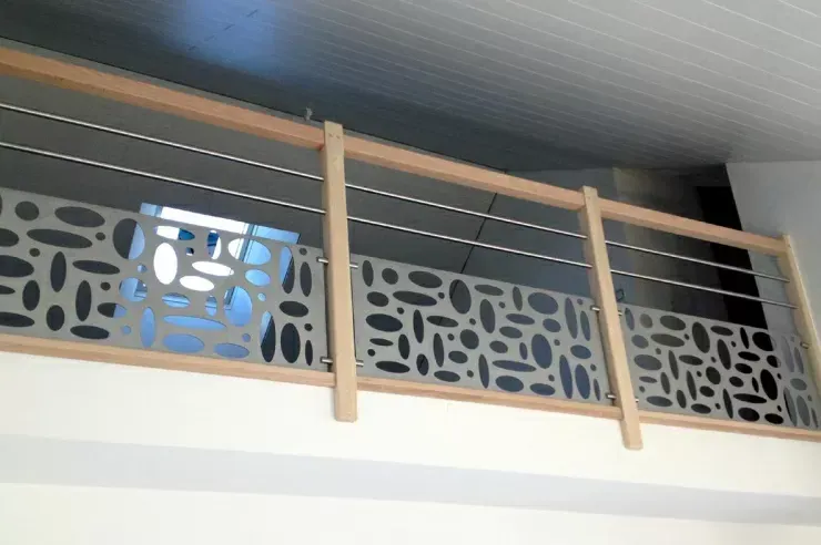 Garde-corps de balcon intérieur avec poteaux en bois, câbles métalliques et panneaux gris à motifs près du plafond