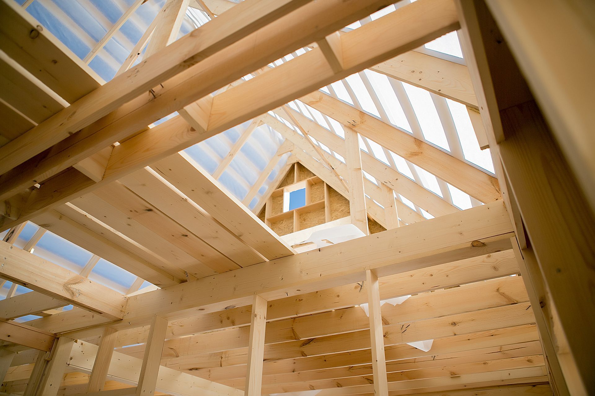 Intérieur d'une maison à ossature en bois en construction, avec poutres apparentes et ouverture pour puits de lumière dans le toit.