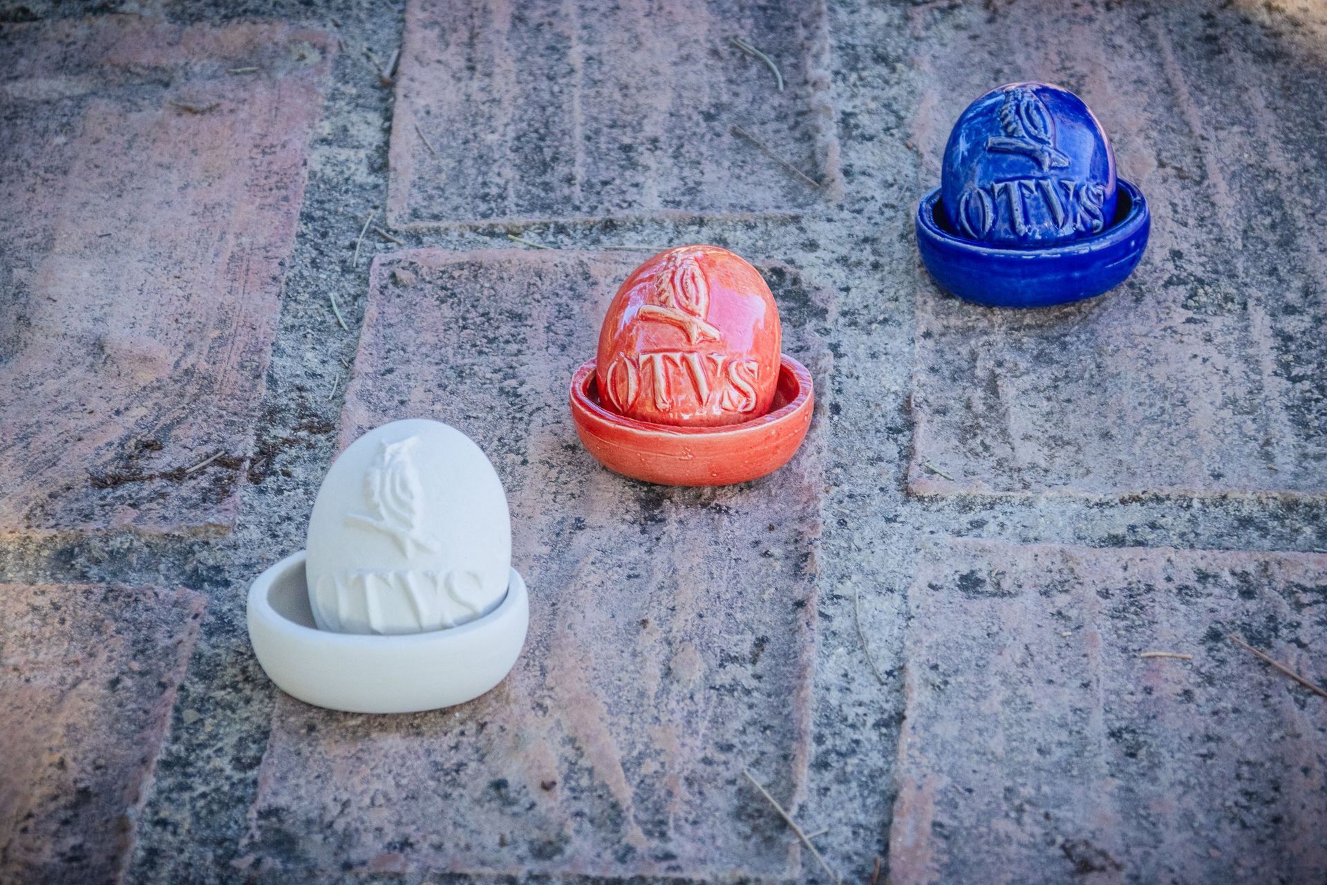 Tres coloridas minifiguras de Buda sobre una superficie de piedra texturizada: blanca, coral y azul.