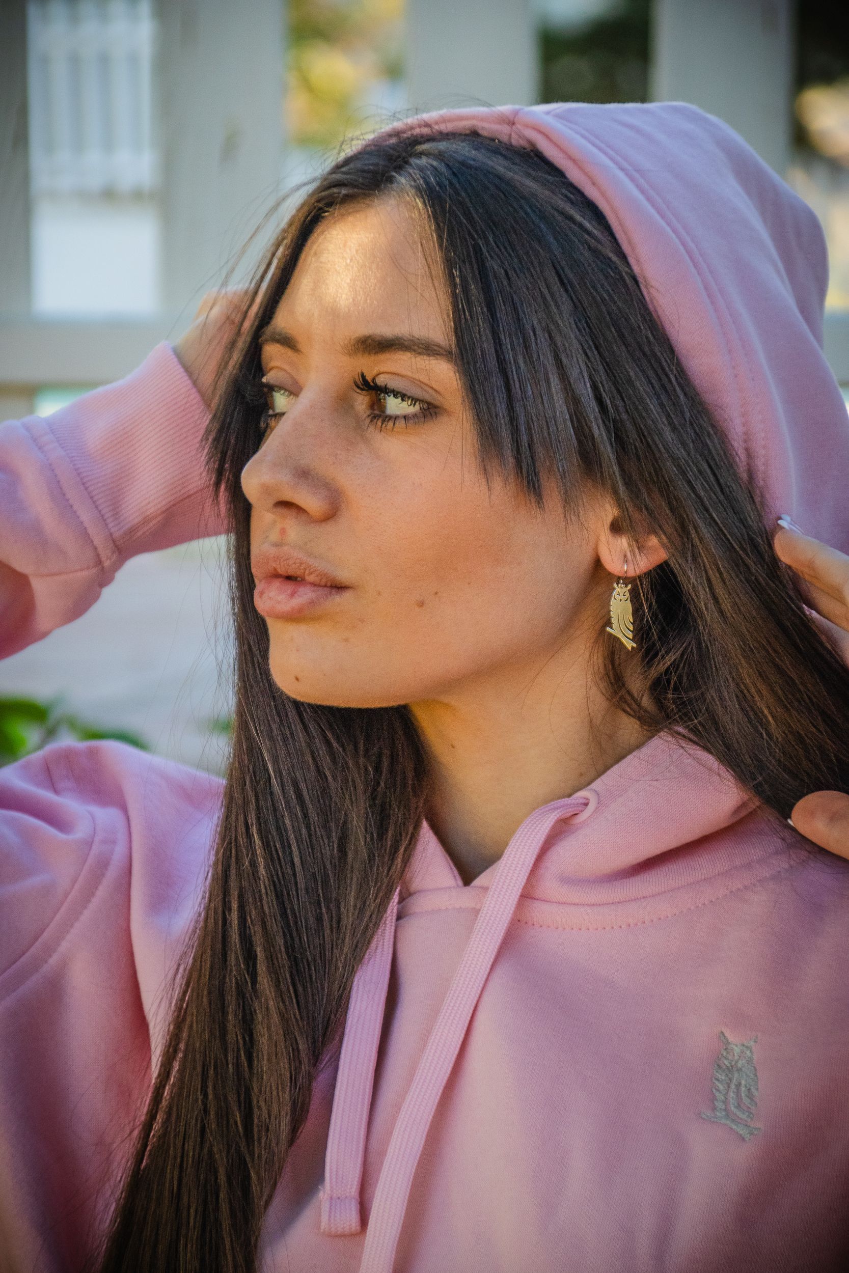 Persona con una sudadera rosa mirando hacia la izquierda, con la mano detrás de la cabeza, al aire libre.