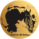 Silueta de búho negro sobre un logotipo circular dorado con el texto “reserva de buhos” en la parte inferior.