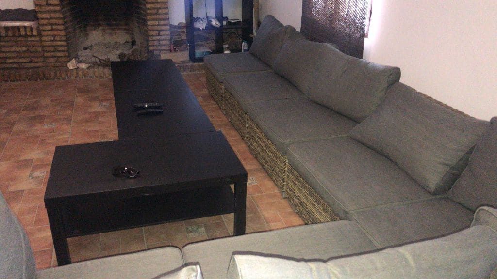 Mesa de centro negra en forma de L junto a un sofá seccional gris en una sala de estar. Se ve una chimenea al fondo.