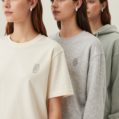 Tres mujeres con camisetas de tonos neutros y una sudadera con capucha, fotografiadas en un estudio minimalista.