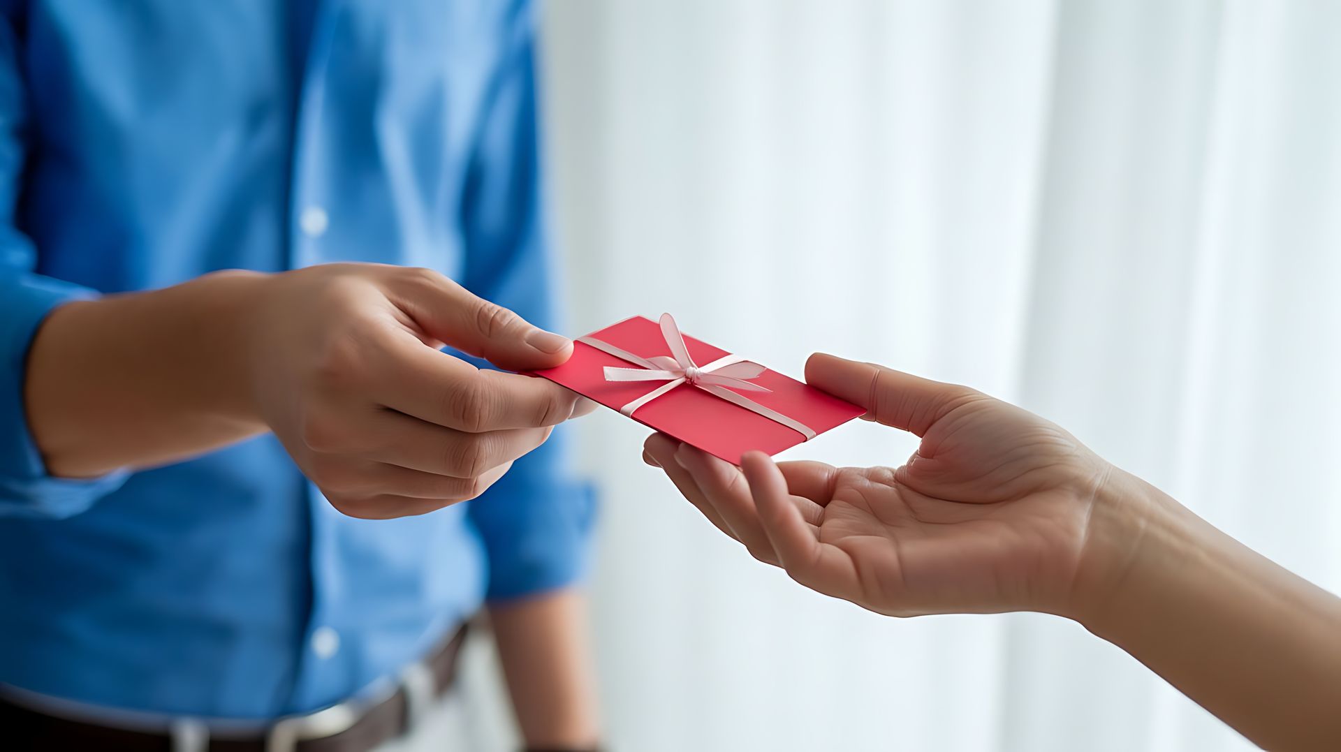 Des mains échangent une carte cadeau avec un ruban blanc.