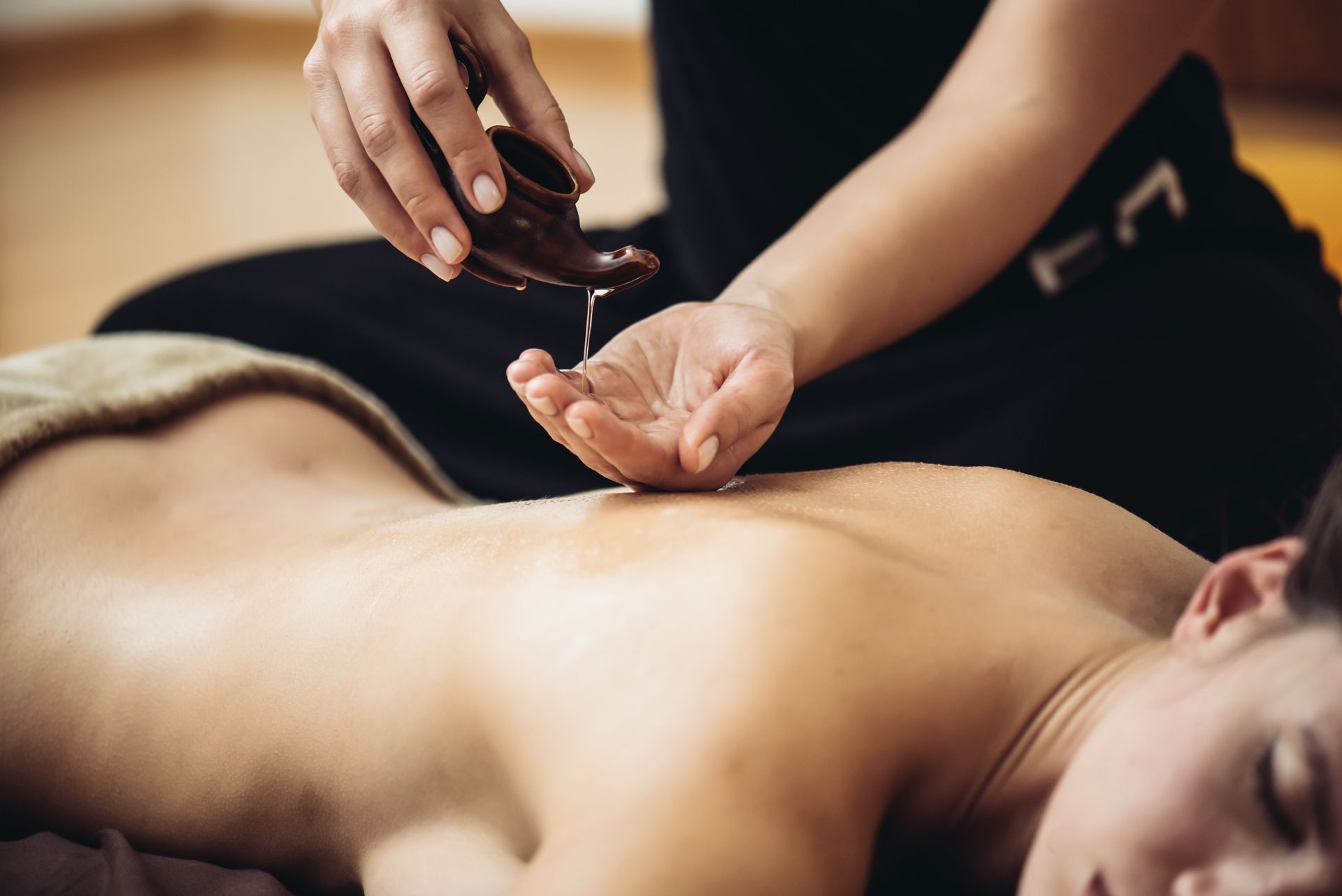Un massothérapeute verse de l'huile sur le dos d'une personne lors d'un massage.