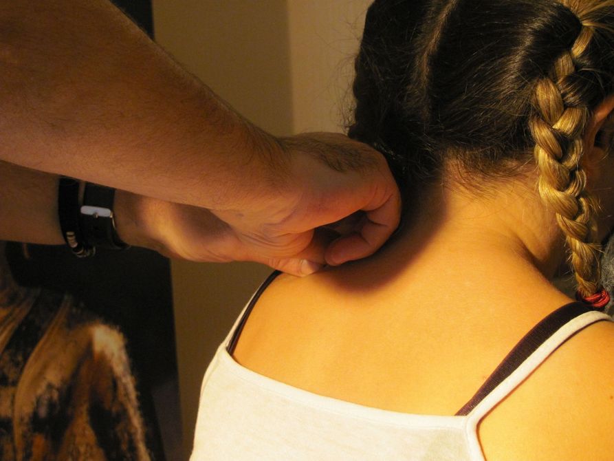 Une personne masse la nuque d'une autre personne assise avec une coiffure tressée.