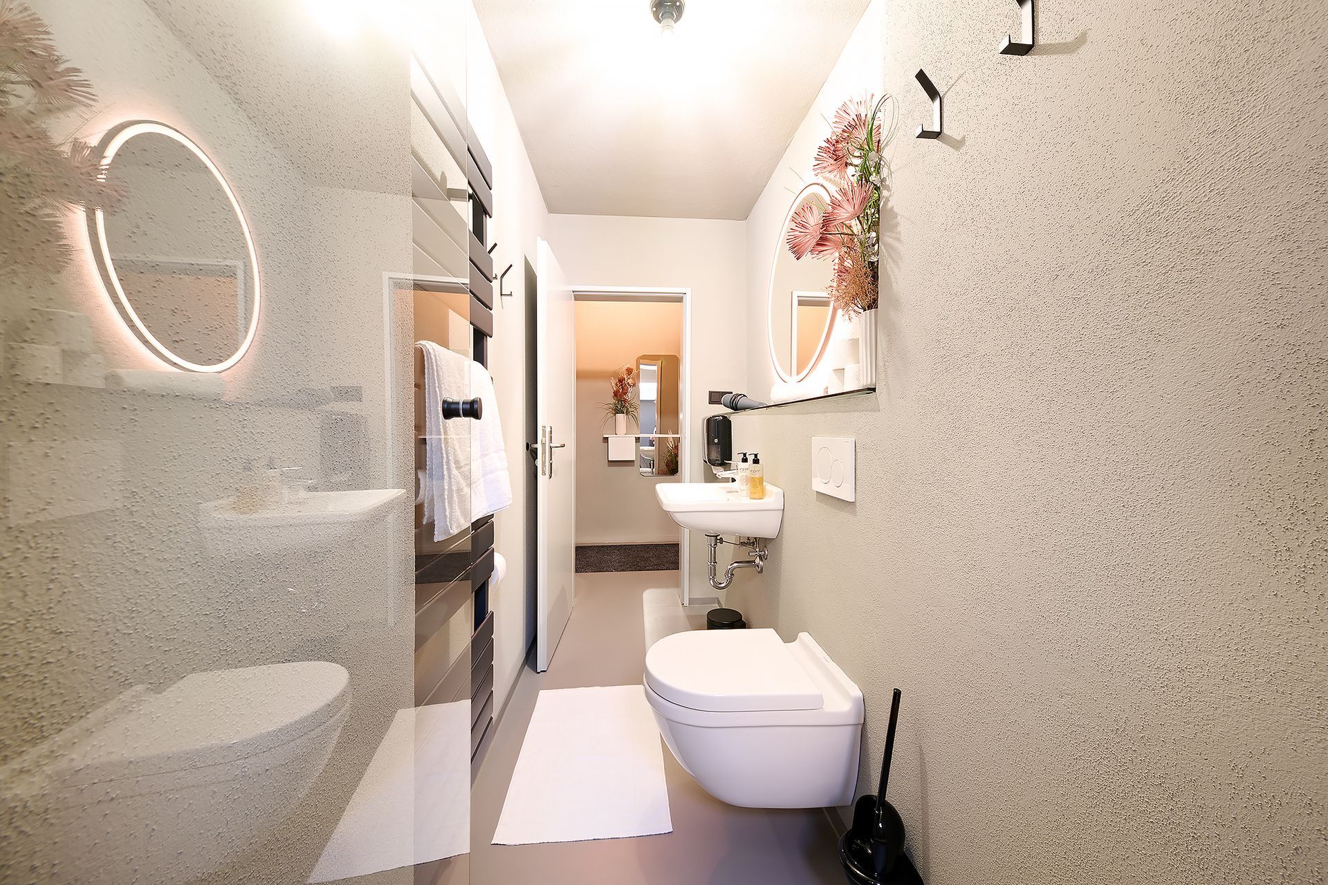 Ein Badezimmer mit Toilette, Waschbecken, Spiegel und ebenerdiger Dusche.