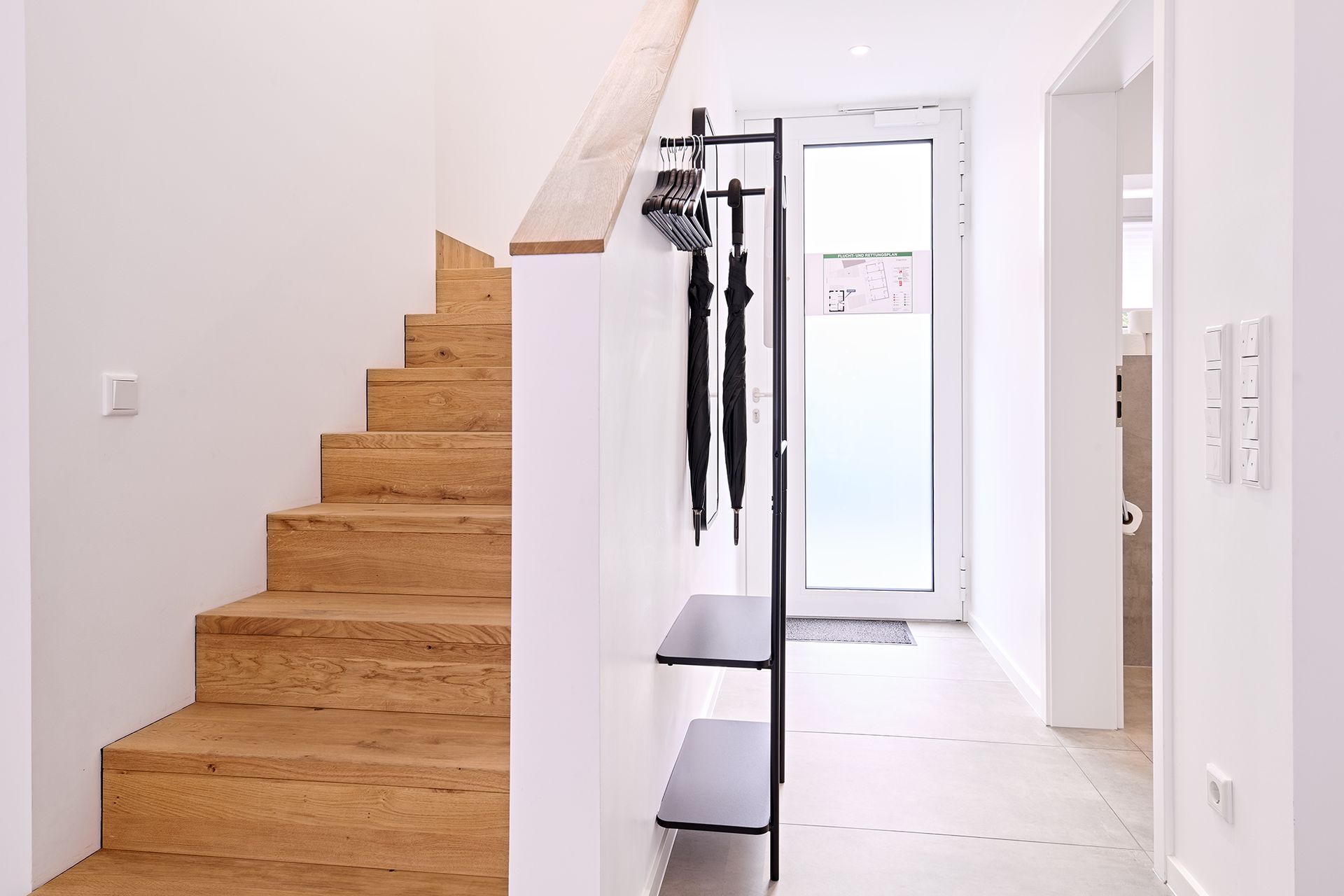 Ein Flur mit Holztreppe und an der Wand hängenden Sonnenschirmen.
