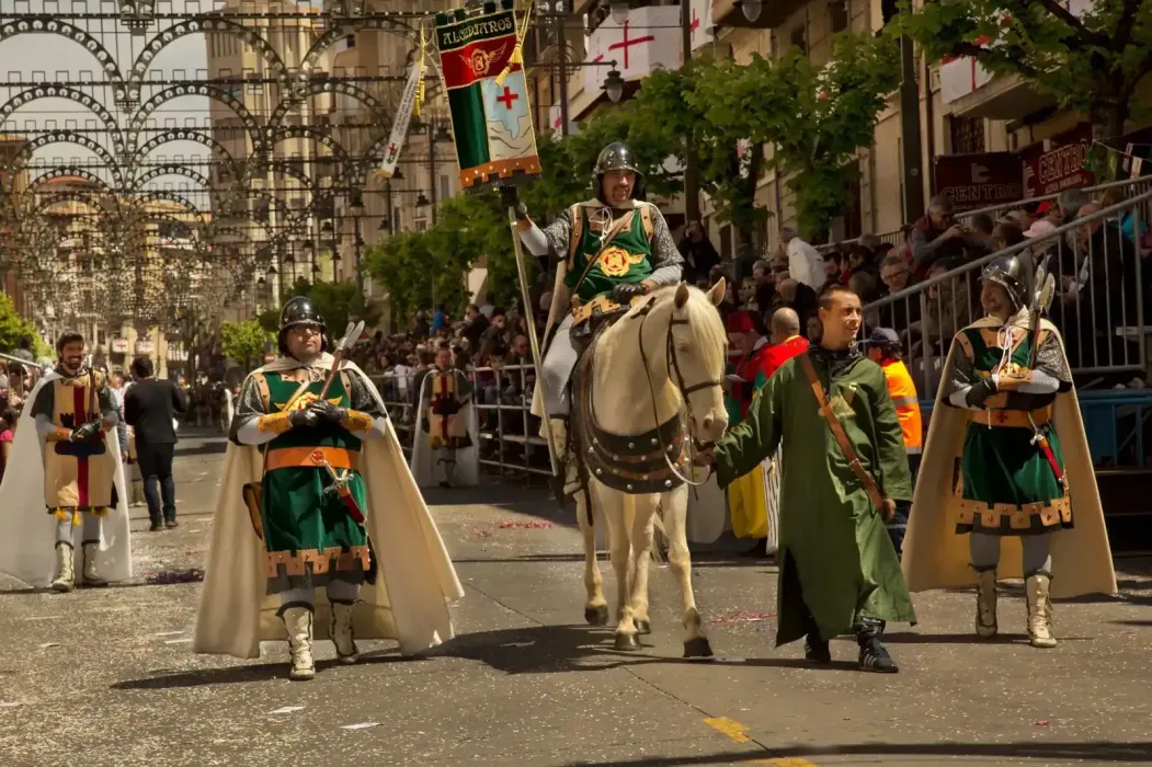 Desfile con figuras disfrazadas, incluido un caballero a caballo, que avanzan por una calle.