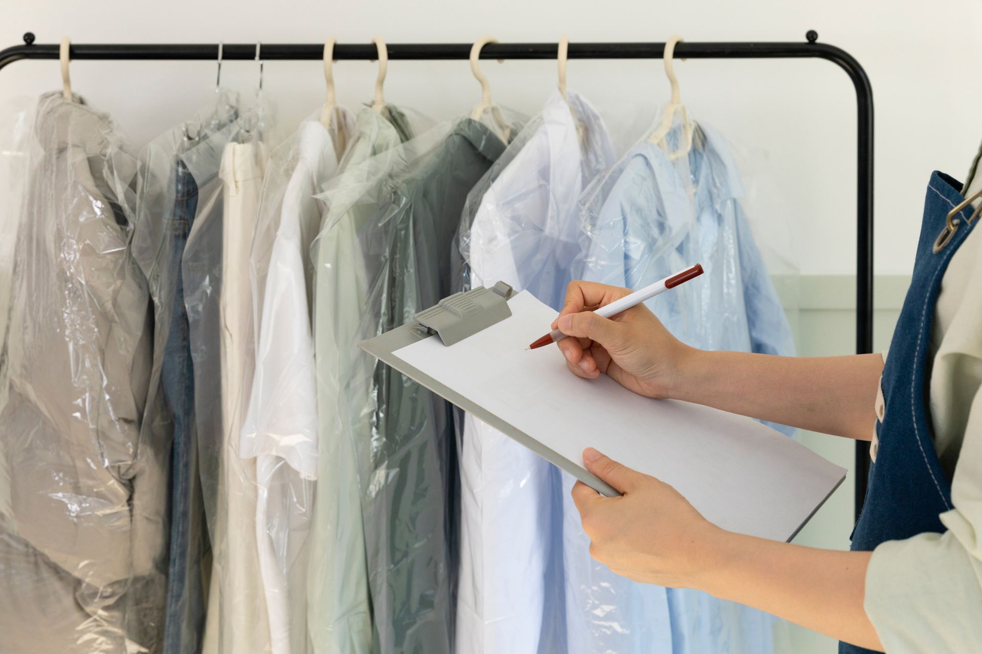 Una persona con portapapeles y bolígrafo registra la ropa colgada en bolsas de plástico en un perchero.