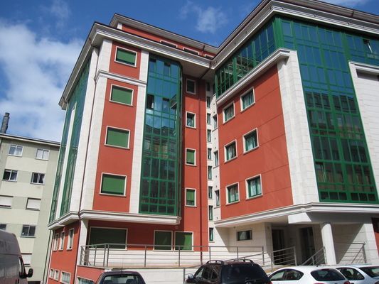 Un gran edificio con muchas ventanas y coches aparcados delante de él.