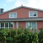 Una casa grande de color rosa con muchas ventanas está rodeada de plantas.