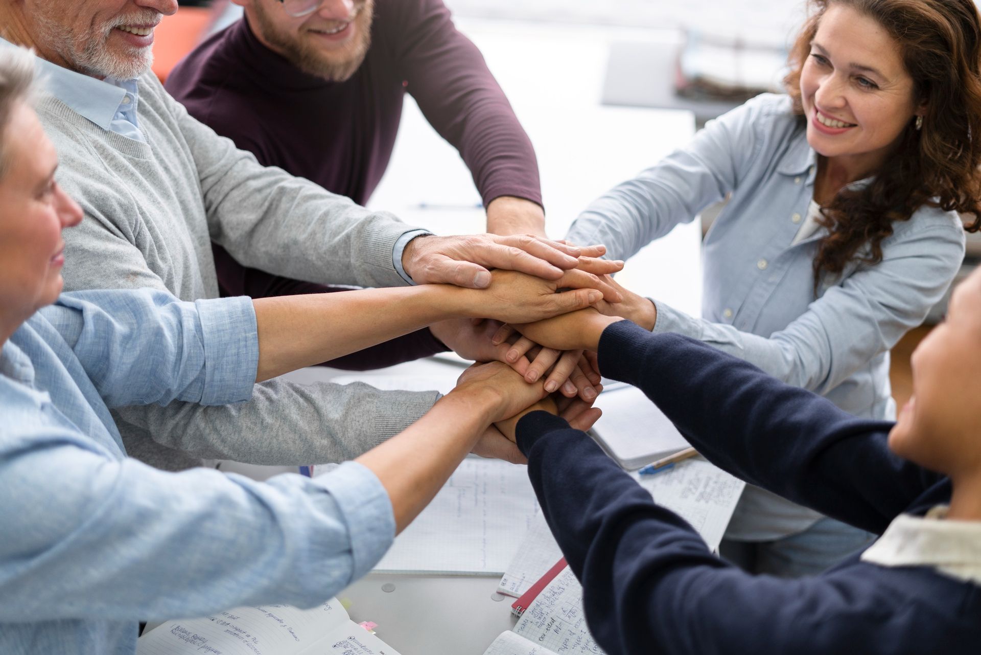 Personas uniendo sus manos en un grupo de equipo, sonriendo, en un espacio interior.