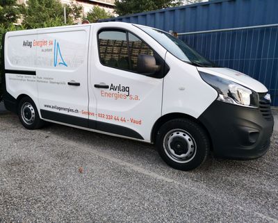Camionnette de livraison blanche avec le logo de l'entreprise garée sur du gravier à côté d'une clôture bleue
