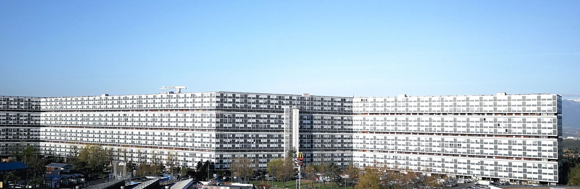 Un vaste immeuble blanc à plusieurs étages se détachant sur un ciel bleu clair.