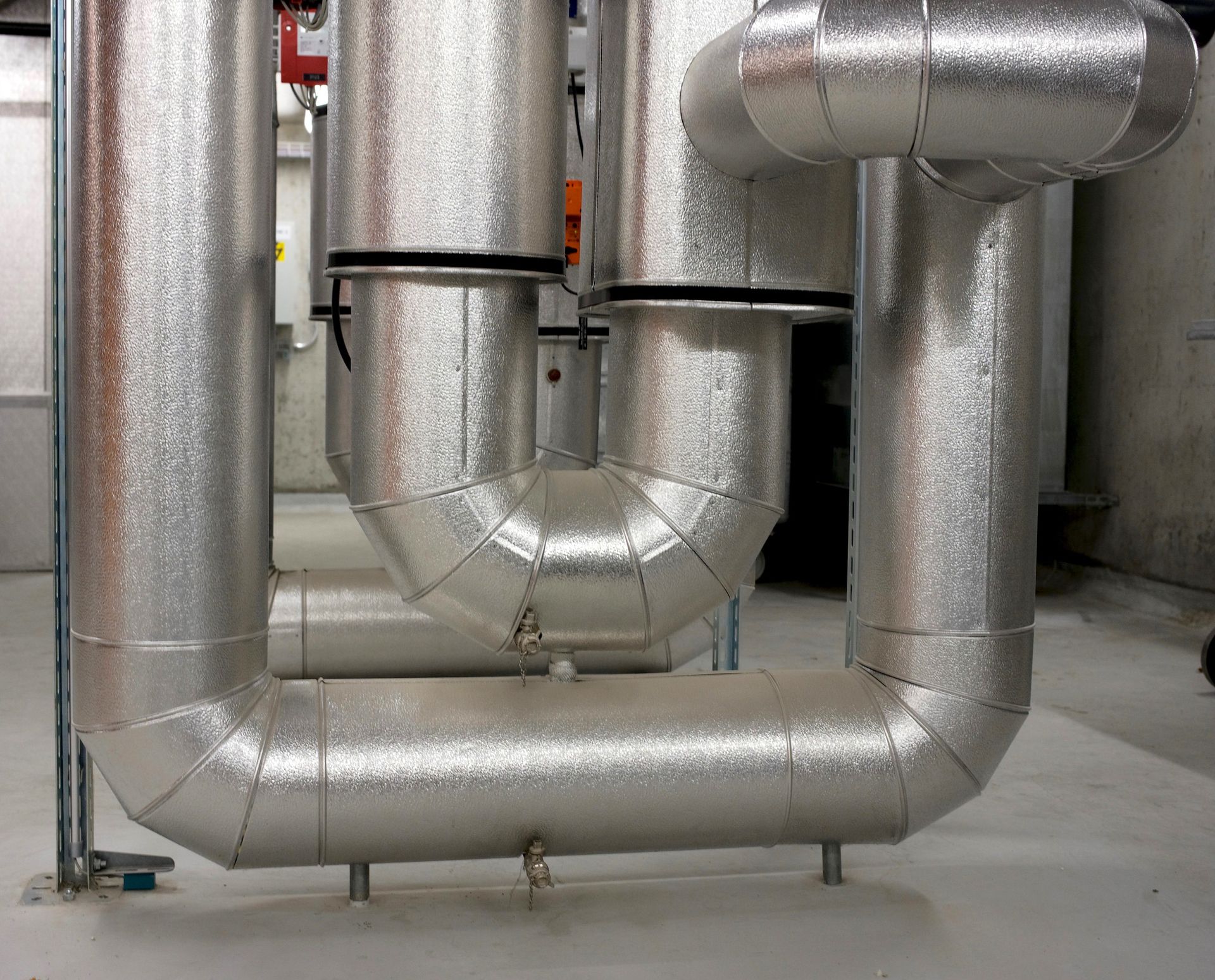 Gros conduits et tuyaux de ventilation isolés argentés dans une salle industrielle.