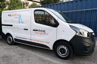 Camionnette de livraison blanche avec le logo de l'entreprise garée sur du gravier à côté d'une clôture bleue