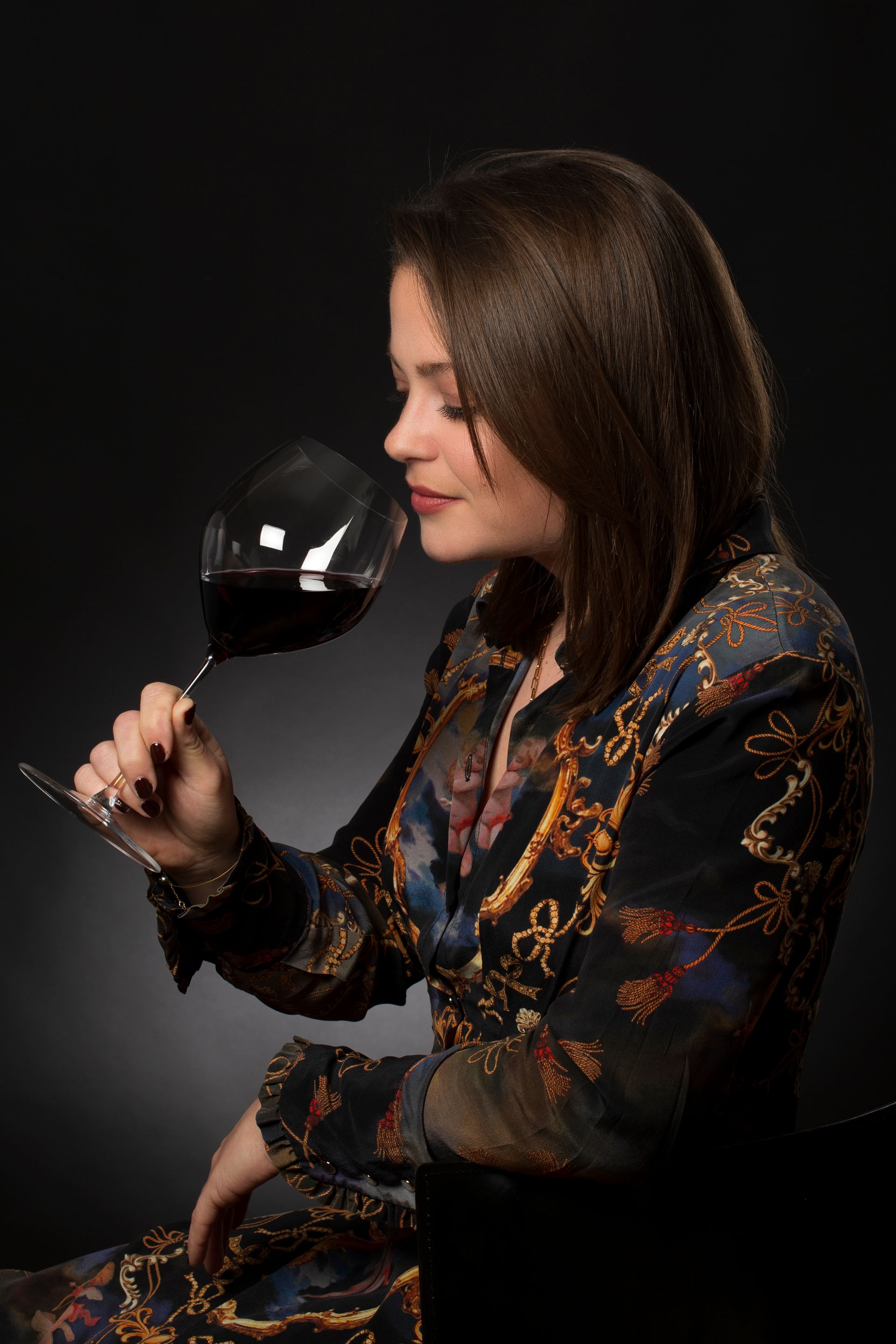 Photo en couleur d'une jeune femme en train de sentir un verre de vin qu'elle tien à la main