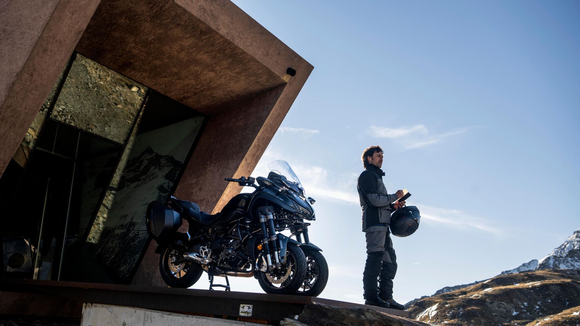Una motocicleta está estacionada al costado de una carretera al lado de una montaña.